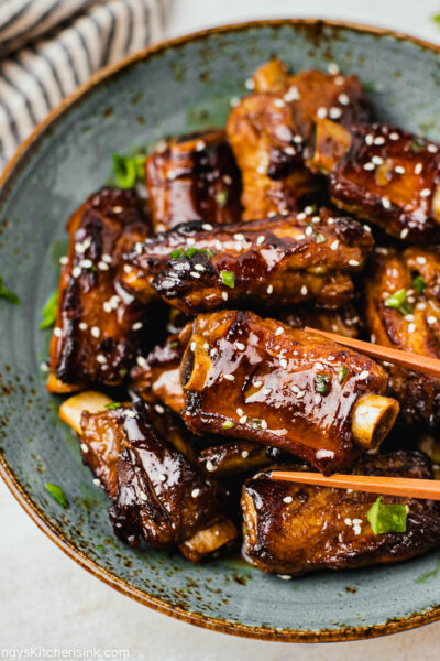 A pair of chopsticks are grabbing a short rib covered in a sticky Asian sauce