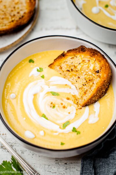 a bowl of creamy and cozy vegan roasted cauliflower pumpkin soup with some gluten free bread in it