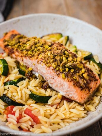 A plate with pasta, veggies, goat cheese, and baked fish with a nutty crust