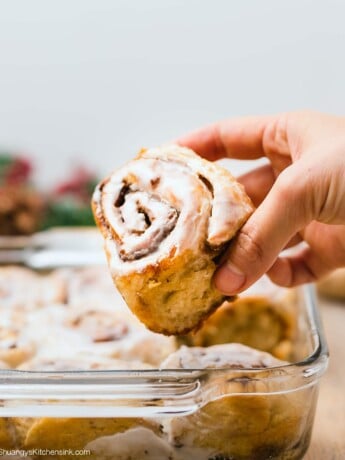 a hand is picking up a freshly baked vegan gingerbread roll iced with dairy-free icing