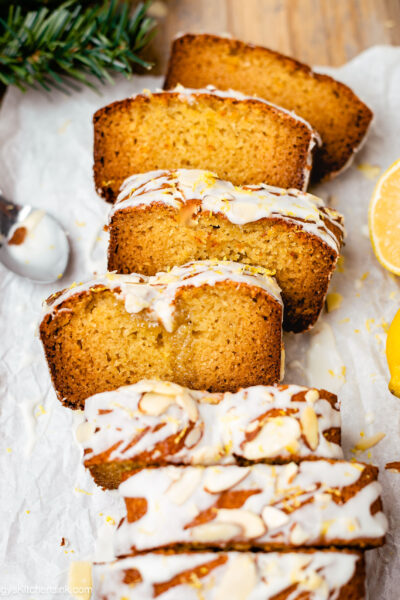 A loaf of soft and moist lemon almond cake topped with limoncello icing. There is a piece of lemon in the background.