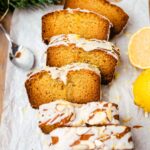 A loaf of soft and moist lemon almond cake topped with limoncello icing. There is a piece of lemon in the background.