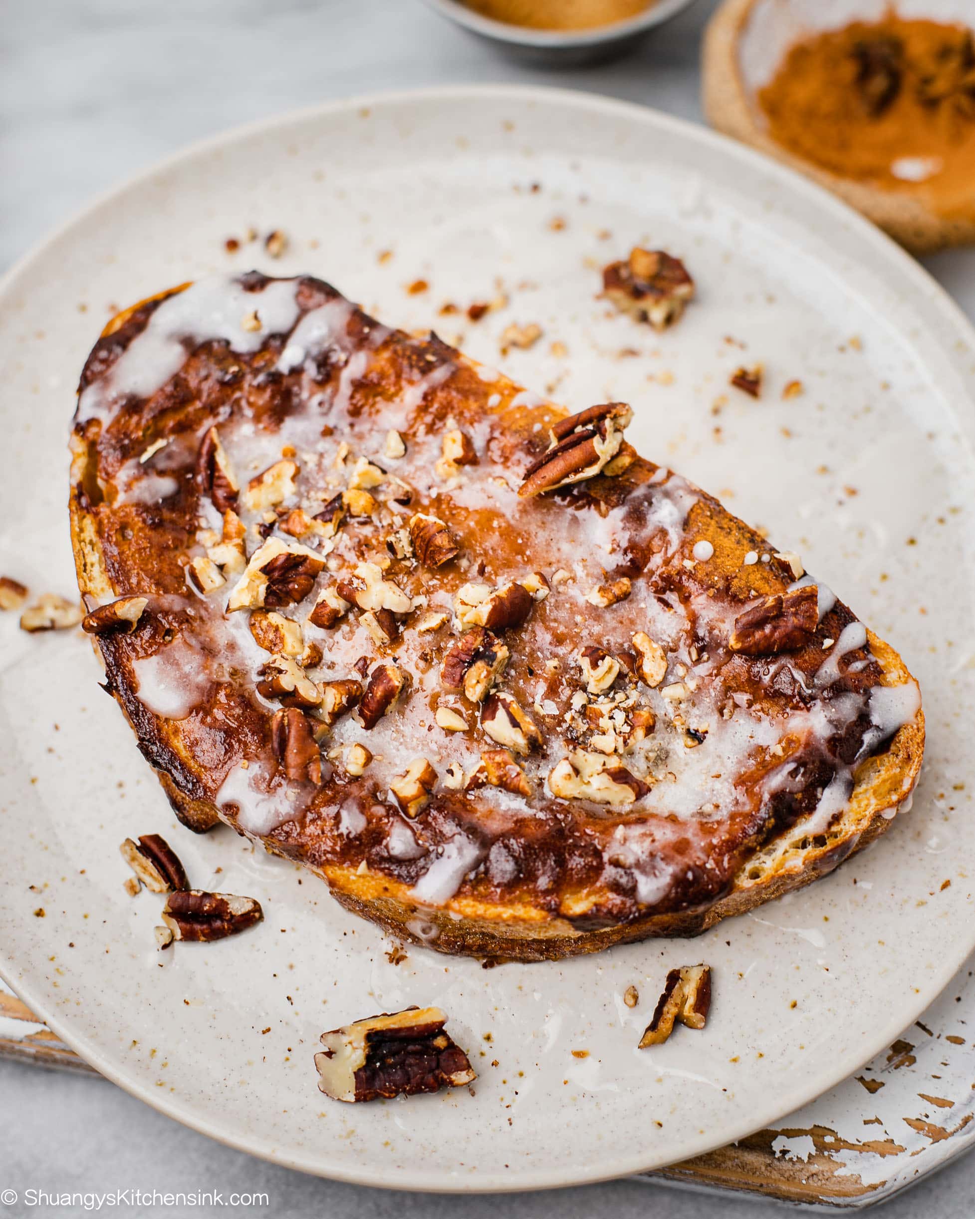 a piece of cinnamon roll custard toast on a cute plate. nuts have been sprinkled on top