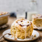 A fluffy banana nut cinnamon roll topped with vegan icing and crushed walnuts