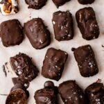 Almond joys fully dipped in chocolate and topped with sea salt sitting on a line cookie sheet