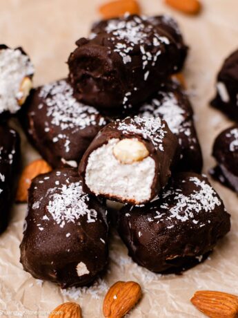 Healthy almond joys sitting in pyramid form on a parchment lined tray- with a bite taken from some of them