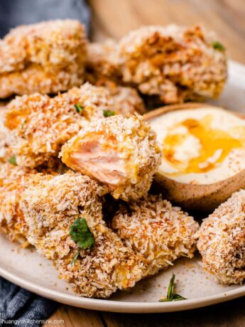 Breaded salmon bites on a plate with a bowl of chipotle honey dipping sauce- one nugget has a bite taken from it