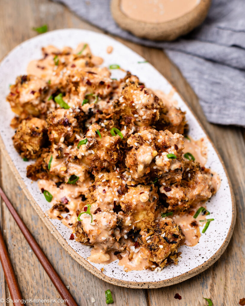 breaded tofu on a plate drizzled with firecracker sauce, topped with chives