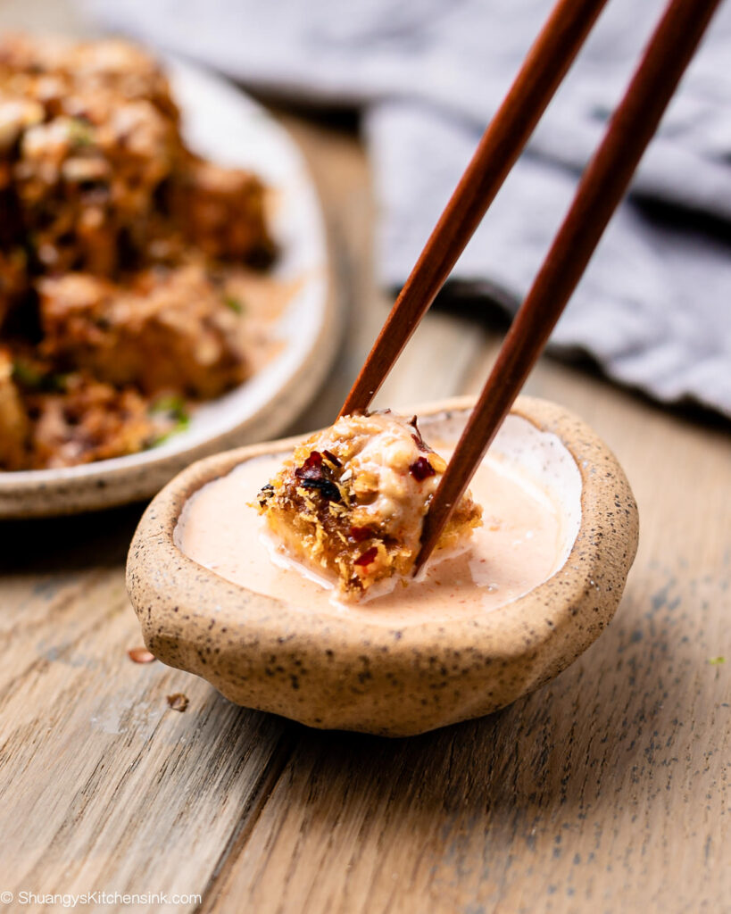 chopsticks dunking the tofu in the firecracker sauce
