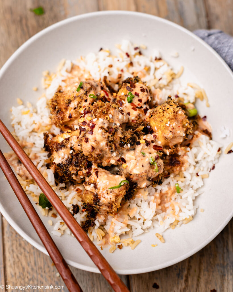 Firecracker Tofu served in a bowl over white rice, with firecracker sauce drizzled on top, and chop sticks sitting on the edge of the bowl