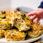 a baby hand is reaching for a blw broccoli and quinoa muffin