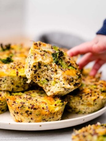 a baby hand is reaching for a blw broccoli and quinoa muffin