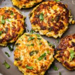 A frying pan with seafood fritters topped with fresh cilantro. There are five of them