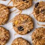 Morning Glory Cookies are sitting on parchment paper and are topped with drizzled nut butter and sea salt