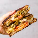 Grilled cheese with chicken pesto has been cooked and grilled to perfection, and is cut in half on a cutting board.