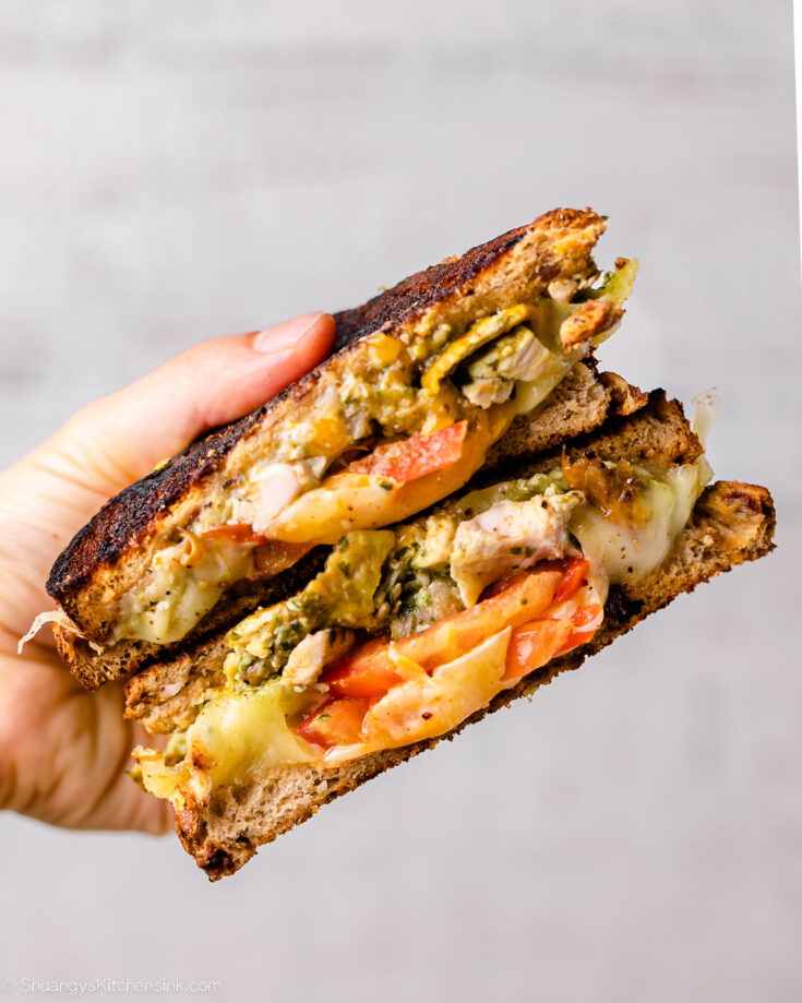 Grilled cheese with chicken pesto has been cooked and grilled to perfection, and is cut in half on a cutting board.