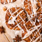 Apple fritters are glazed with an apple spice glaze sitting on parchment paper, and star anise is used as decor.