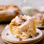 A fluffy caramel apple cinnamon roll topped with vegan icing and crushed pecans