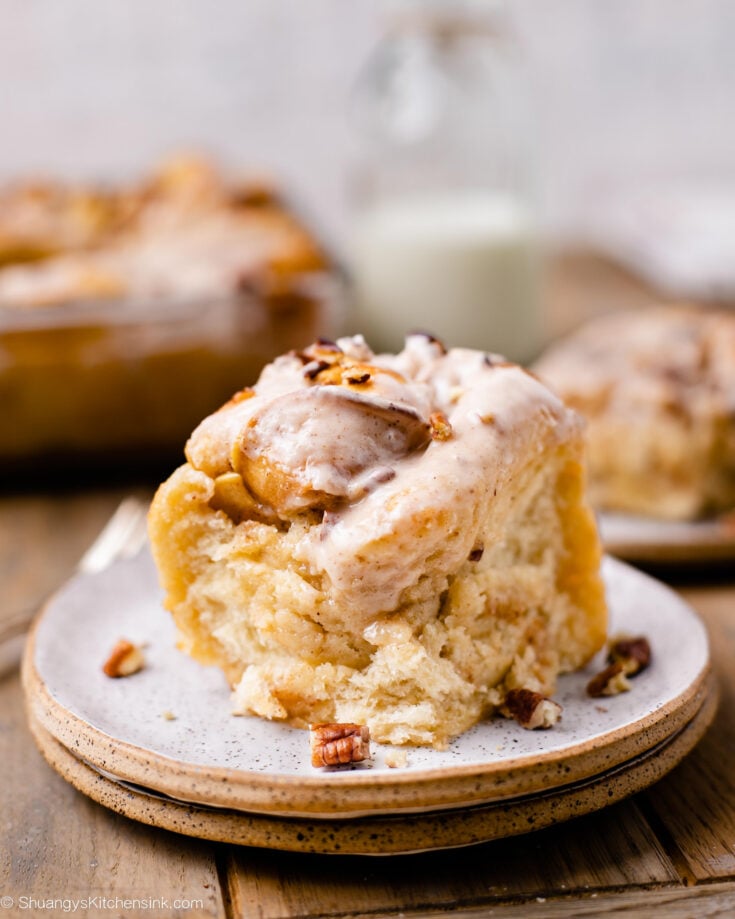 A fluffy caramel apple cinnamon roll topped with vegan icing and crushed pecans