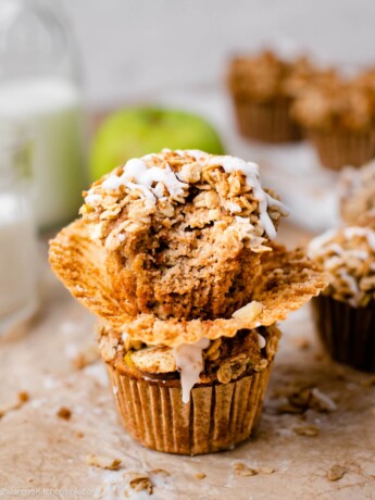 Two apple crumb muffins stacked on top of eachother, and a bite taken from one.