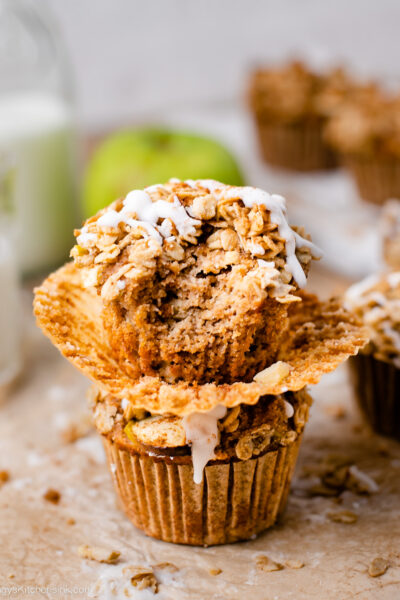 Two apple crumb muffins stacked on top of eachother, and a bite taken from one.