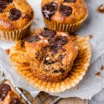 There is a muffin with a bite taken from it. It looks soft and moist and the banana muffin is paleo and gluten-free and topped with vegan chocolate chips