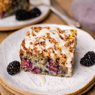 A square of the coffee cake has blackberry swirl and glaze on top, while sitting on a stack of small plates