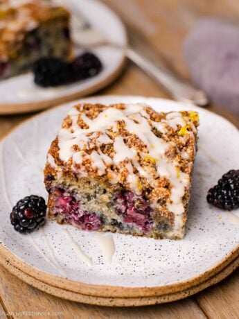 A square of the coffee cake has blackberry swirl and glaze on top, while sitting on a stack of small plates