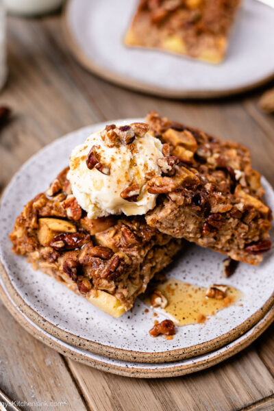 Apple butter baked oats are being served on a small plate with icecream and drizzled with maple syrup
