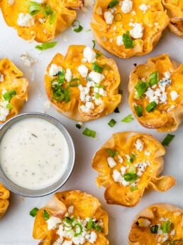 crispy wonton appetizers garnished with blue cheese crumbles, being served with a ranch dressing