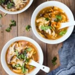 Hot and sour soup is being served in little soup bowls with spoons- topped with cilantro