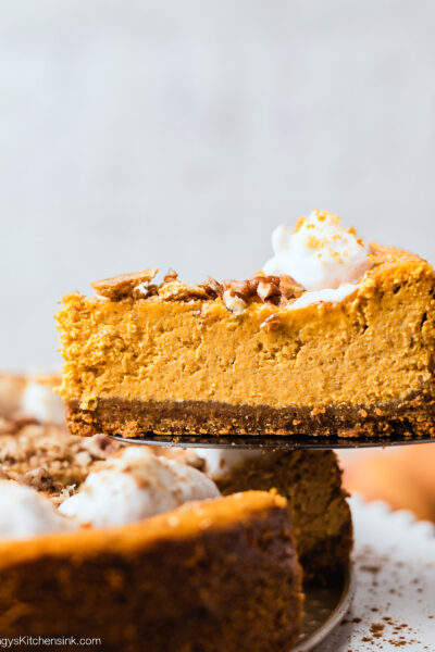 A slice of pumpkin cheesecake has been cut, and is being held on a pie cutter