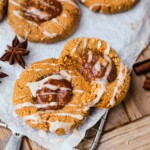 Pumpkin thumbprint cookies are sitting on parchment paper and have a glaze drizzled on top of them.