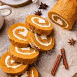 Pumpkin Roll with vegan cream cheese filling is perfectly sliced on parchment and dusted with powdered sugar.