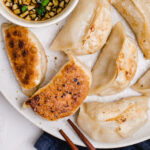 Potstickers have a golden brown char on their bottoms and are being served on a plate along with garlic ginger asian sauce