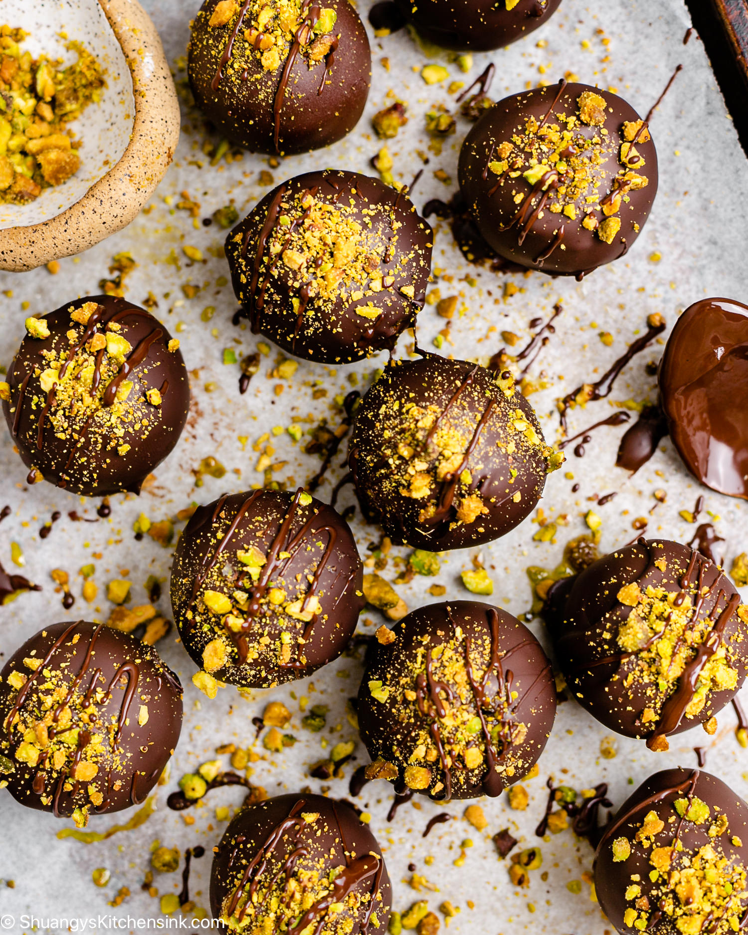 Pistachio truffles are coated in chocolate and crushed pistachio on a parchment lined cookie sheet.