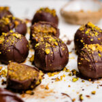No bake pistachio truffles are laying on a parchment lined sheet, with pistachios crumbled around,