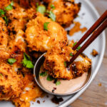 Crispy breaded chicken bite being dipped into a creamy sriracha mayo sauce with chopsticks, shown close-up