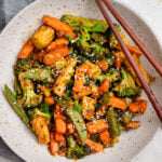 Veggie stirfry is served on a plate with sesame seed.