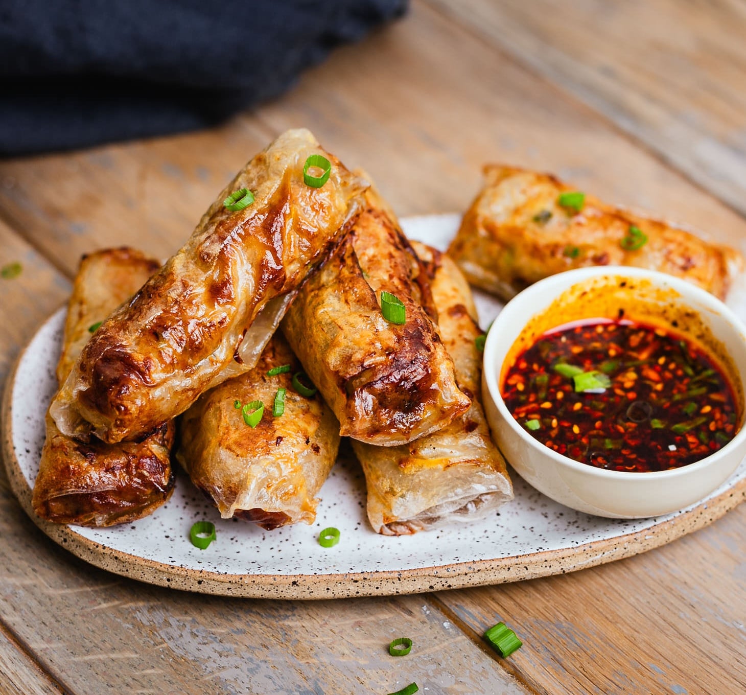 a plate of air fried rice paper spring rolls with a dish of chili oil on the side. There are some scallions on top.