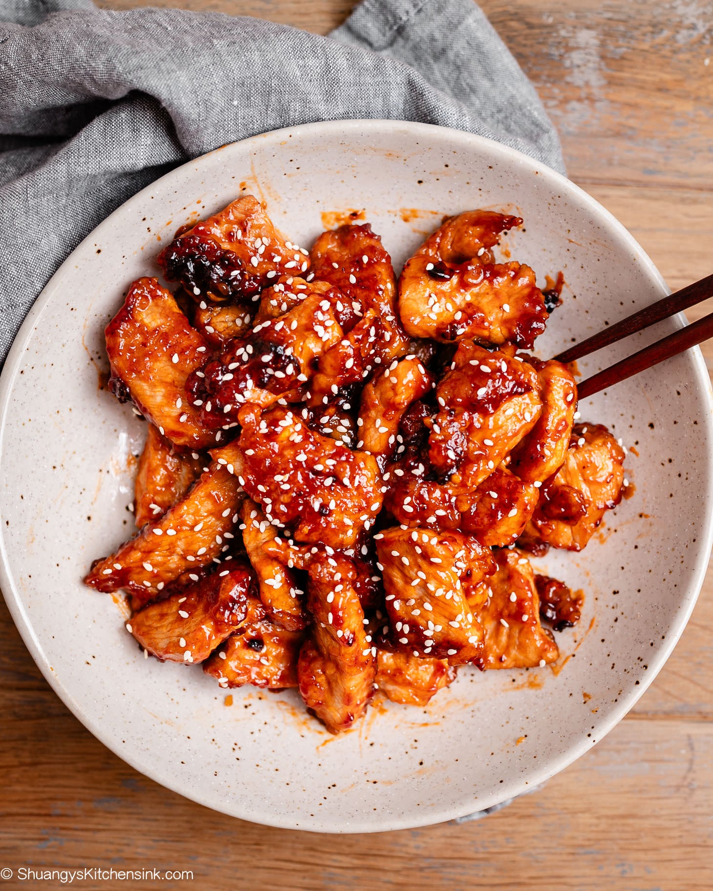 Pan-fried sweet and sour pork on a plate, garnished with sesame seeds and chopped green onions, ready for a family dinner.