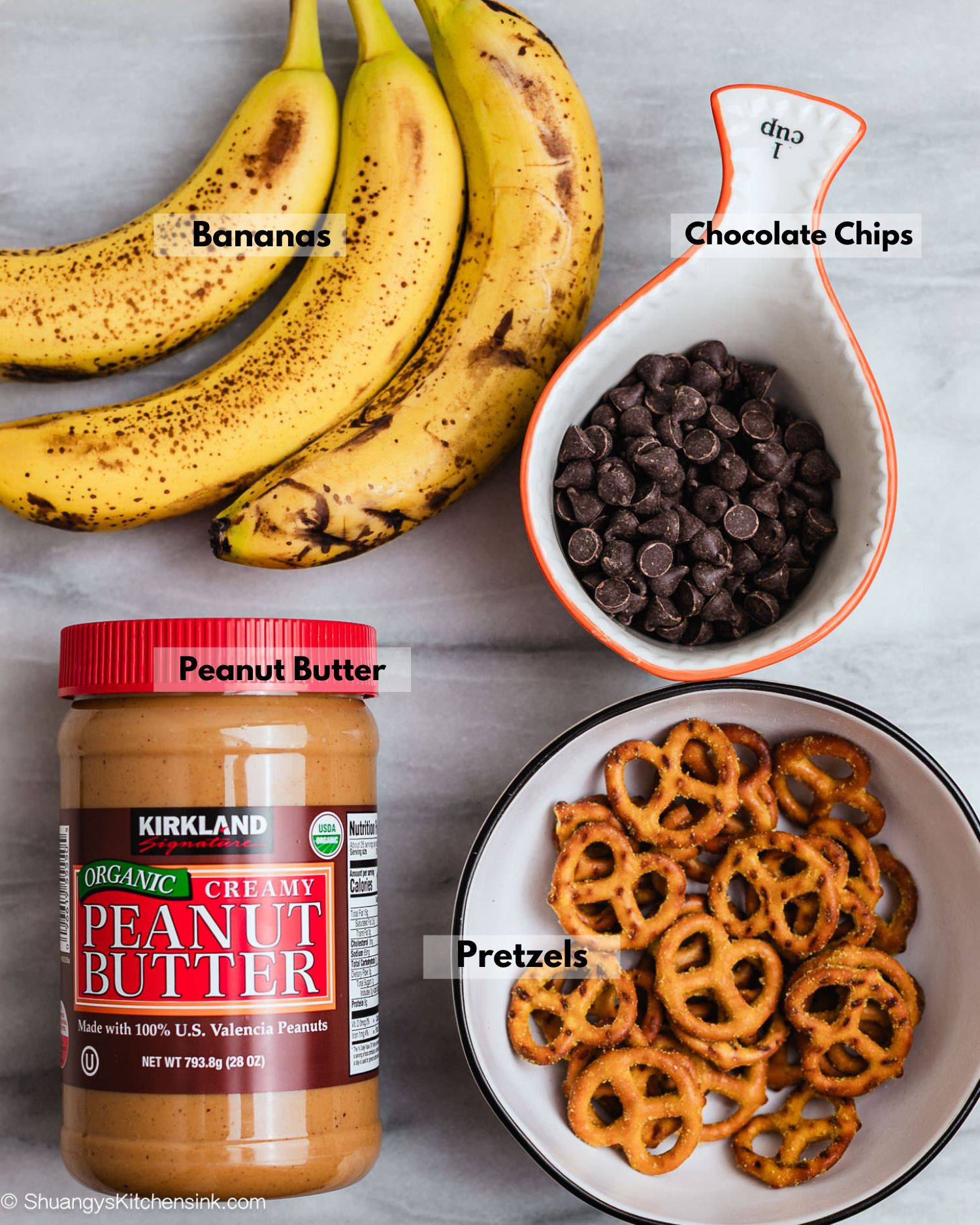 Ingredients for Frozen peanut butter banana bites made with banana slices, pretzels, creamy peanut butter, and a drizzle of melted dark chocolate, sprinkled with sea salt.