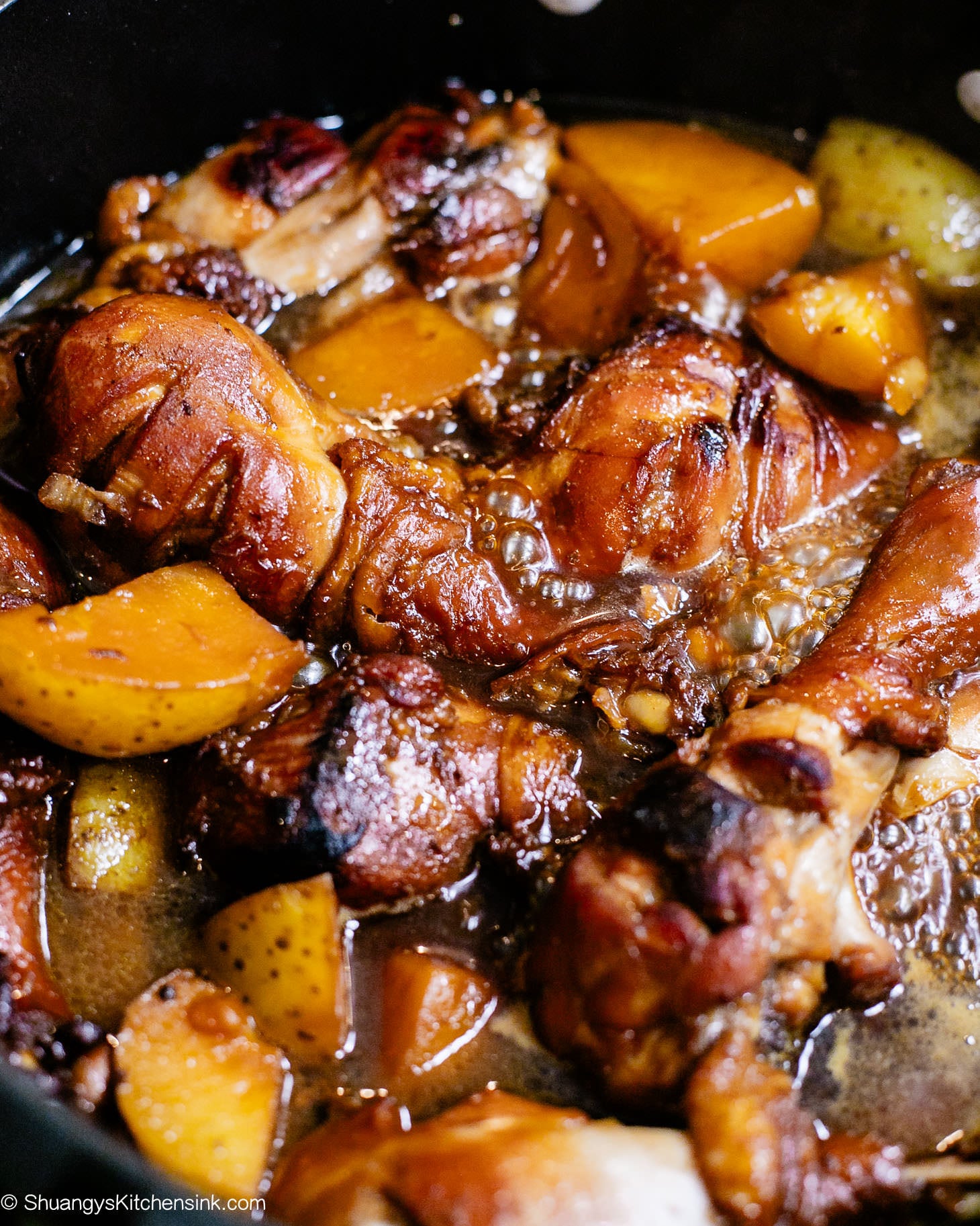 A pot of red braised chicken drumsticks, they are seared on top to caramelized golden brown. There are also potatoes in the pot.