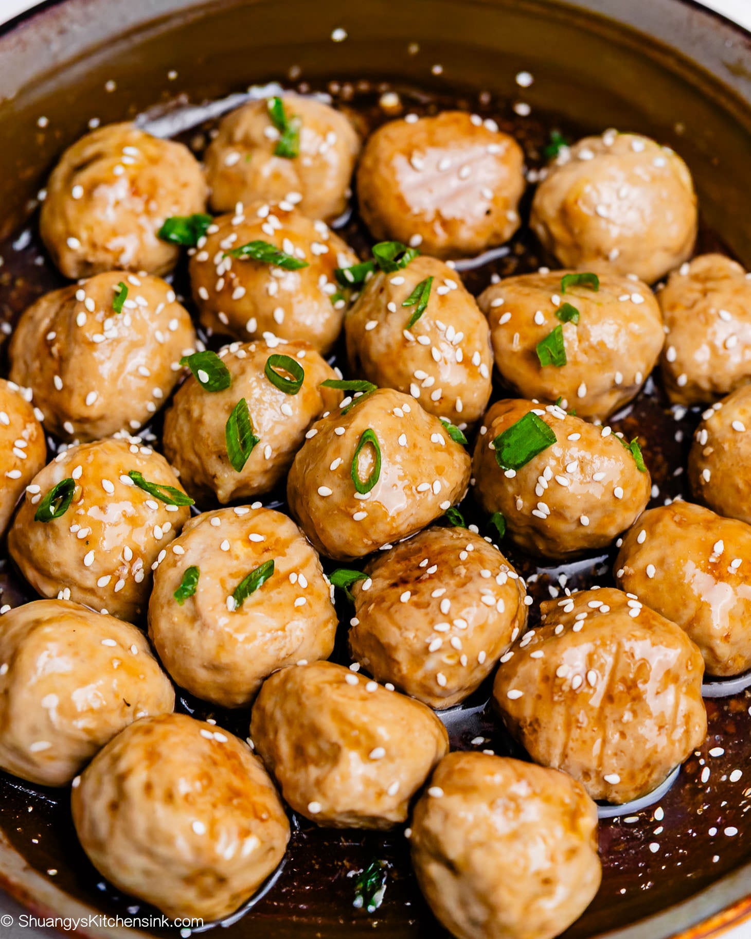 Juicy honey garlic meatballs simmered in sauce, topped with sesame seeds and chopped scallions in a skillet.