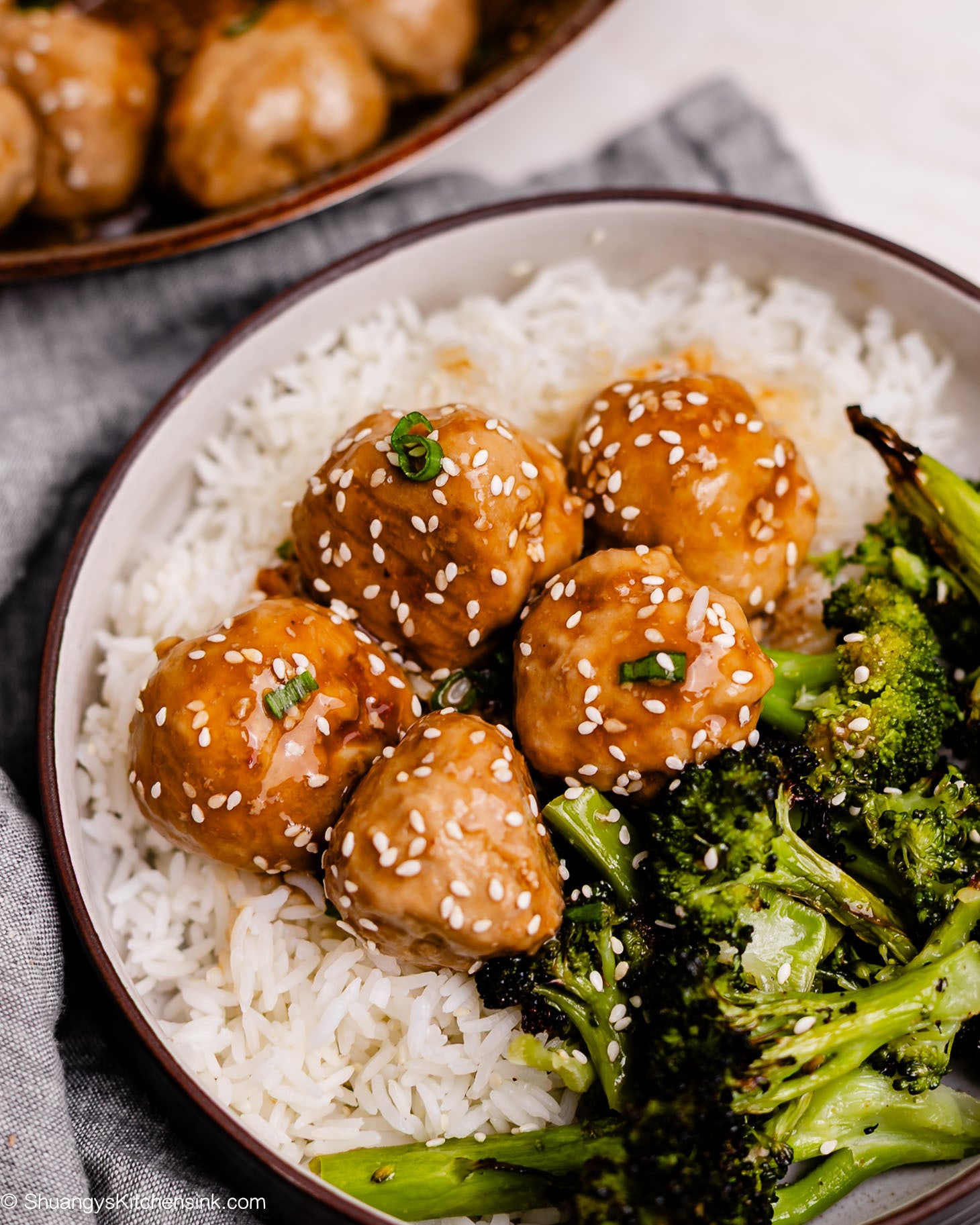 Bowl of honey garlic meatballs served with jasmine rice and roasted broccoli, garnished with sesame seeds and scallions.