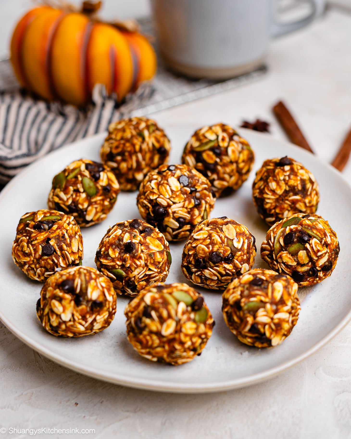 A plate of no-bake pumpkin energy balls made with oats, pumpkin puree, peanut butter, chocolate chips, and pumpkin seeds, stacked neatly with a cozy fall background.