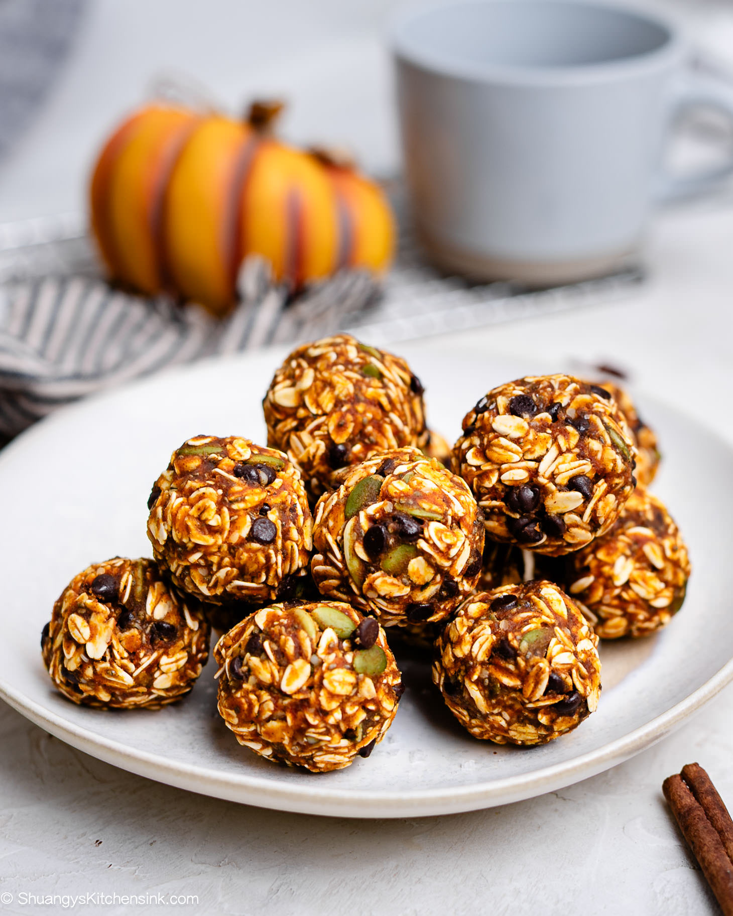 A plate of no-bake pumpkin energy balls made with oats, pumpkin puree, peanut butter, chocolate chips, and pumpkin seeds, stacked neatly with a cozy fall background.