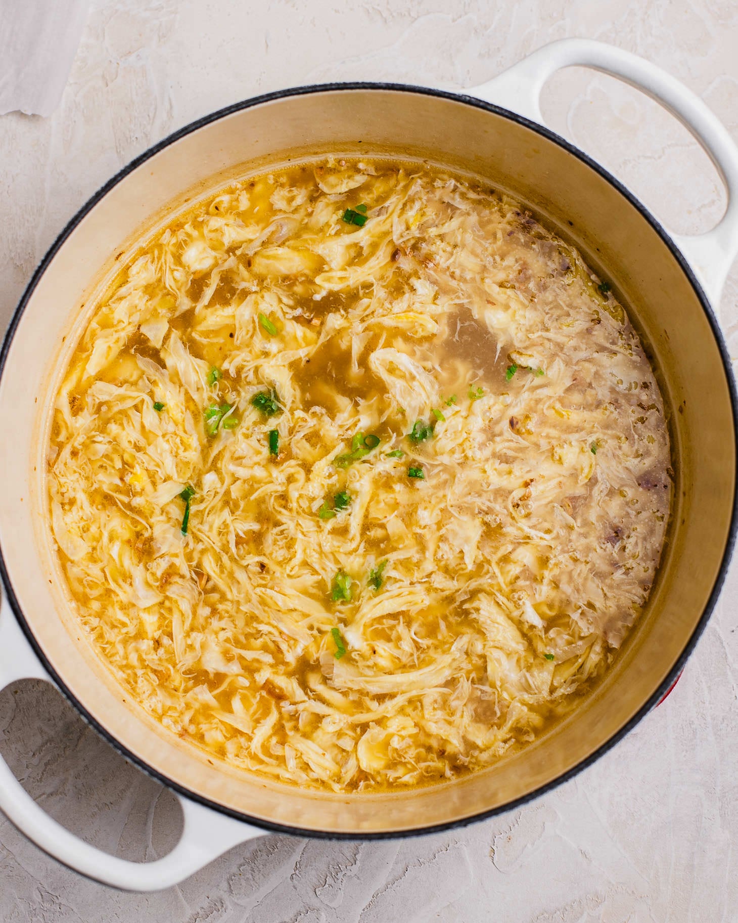 Silky egg drop soup with soft egg ribbons in a big pot. it is topped with chopped scallions
