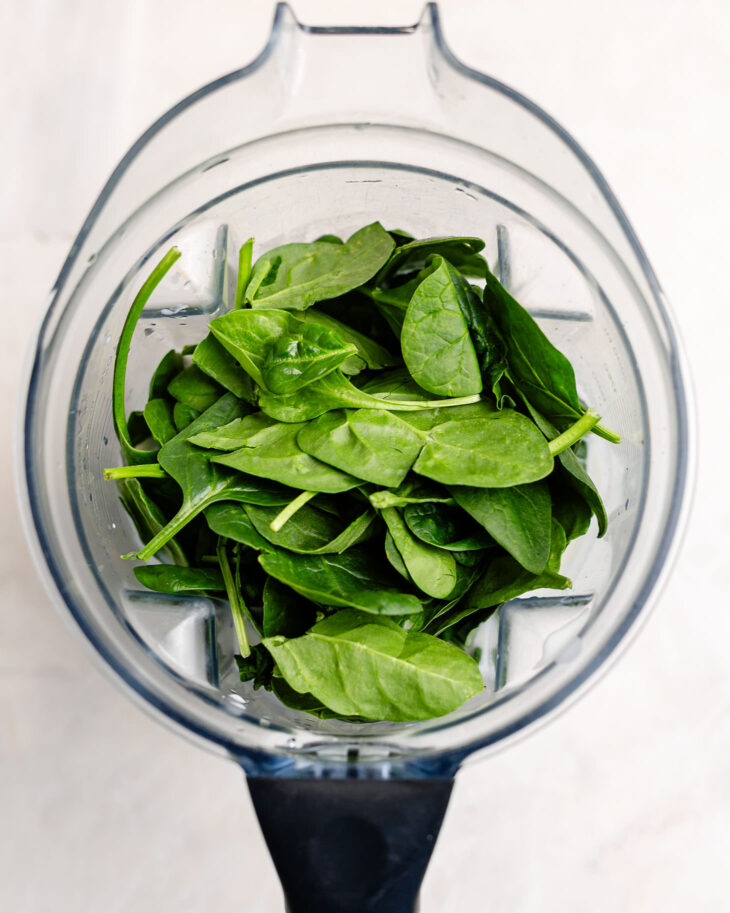 Fresh baby spinach added to a high-speed blender as the first step in making a kid-friendly green smoothie for homemade smoothie pouches.