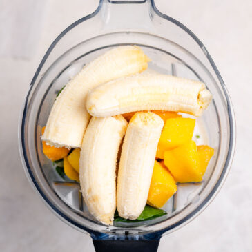 Bananas and frozen mango added to spinach and milk in a blender to make a creamy spinach smoothie for kids.